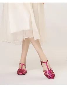 Close-up of woven metallic rose red T-strap sandals worn with a white dress