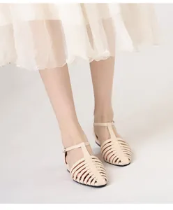 Close-up of beige woven leather Roman sandals paired with a cream pleated chiffon skirt