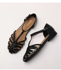Detail view of woven leather texture and T-strap metal buckle on black retro sandals