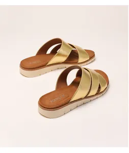 Close-up of golden metallic crisscross straps and thick non-slip sole on women's slides