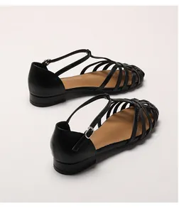 Detail view of woven leather texture and metal buckle on black T-strap flat sandals