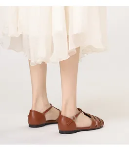 Gros plan de sandales plates romaines en cuir marron avec bride en T et boucle