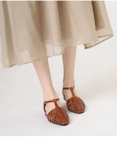 Close-up of brown woven T-strap Roman sandals with hollow leather texture and metal buckle