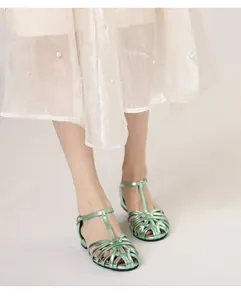Close-up of light green woven T-strap sandals with metallic finish and buckle strap