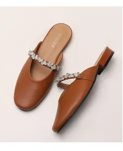 Close-up of caramel brown leather mules with sparkling rhinestone strap detail and round toe