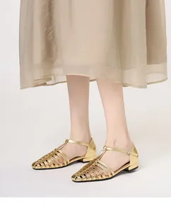 Detail of gold woven roman sandals with T-strap and buckle closure on model
