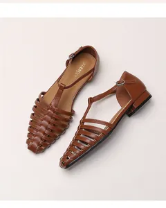 Close-up of brown leather woven sandals with T-strap and metal buckle detail