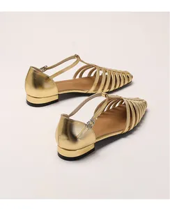 Close-up of golden woven leather flat sandals with T-strap buckle and metallic finish
