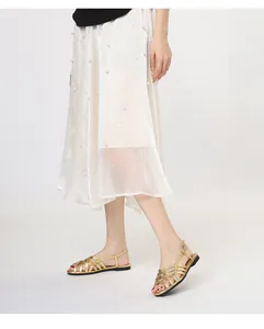 Close-up of golden woven strap sandals on model paired with elegant pleated skirt