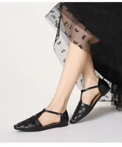 Detail van zwarte gevlochten platte sandalen met T-riempje en stijlvolle open teen