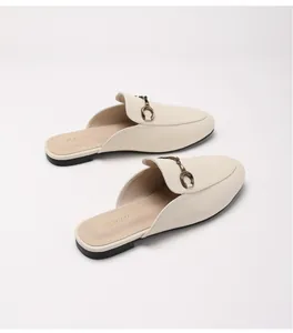 Λεπτομέρεια από μπεζ φλατ mules με vintage μεταλλική αγκράφα και στρογγυλεμένη μύτη