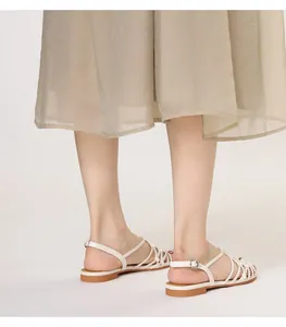 Detail view of woven straps and silver buckle on cream flat Roman sandals