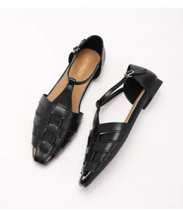 Detail van zwarte gevlochten platte T-strap sandalen met retro vierkante neus en gesp