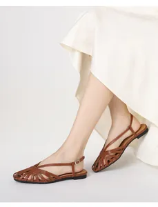 Close-up van bruine gevlochten sandalen met fijne enkelbandjes en verstelbare gesp