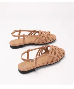 Detailed close-up of woven strappy upper and adjustable buckle on apricot flat sandals