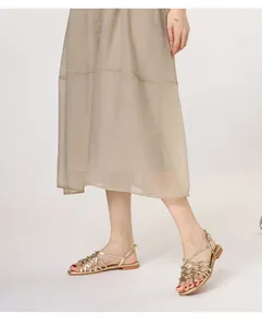 Detail of woven metallic gold straps on flat Roman sandals with minimalist ankle wrap