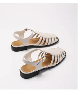 Close-up of cream woven leather hollow-out sandals with black flat sole and buckle