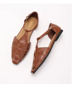 Detail van bruine handgevlochten leren sandalen met T-strap en zilveren gesp op witte achtergrond