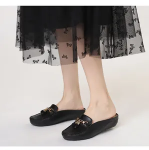 Dettaglio di sabot in pelle nera con fibbia a morsetto dorata e nappine decorative