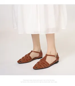 Detail van bruine geweven leren sandalen met T-bandje en metalen gesp aan de voet van een model