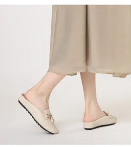 Vista laterale di sabot beige con fibbia dorata, frange e lati con micro fori