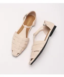 Detailopname van de geweven vierkante neus en T-sluiting op beige platte romeinse sandalen