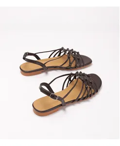 Detail view of dark brown woven straps and metal buckle on women's flat Roman sandals