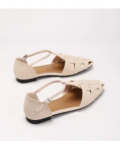 Detail van beige gevlochten platte sandalen met T-strap en metalen gesp