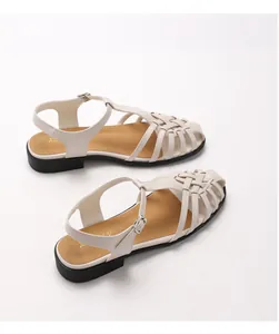 Detail der cremefarbenen geflochtenen Römersandalen mit brauner Sohle und Metallschnalle am Riemen