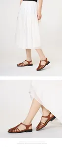 Details brauner geflochtener Römersandalen mit T-Riemchen und schickem Faltenrock