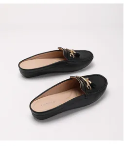 Dettaglio di sabot in pelle nera con trafori decorativi, fibbia dorata e nappe eleganti