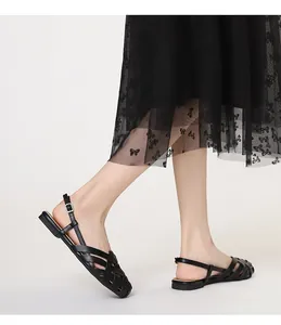 Detalle lateral de sandalias negras tejidas planas con diseño calado y hebilla ajustable