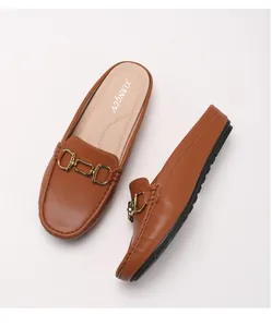 Λεπτομέρεια από καφέ δερμάτινα loafers με χρυσή μεταλλική αγκράφα σε λευκό φόντο