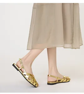 Detalle de sandalias planas doradas trenzadas con diseño hueco y correa de hebilla
