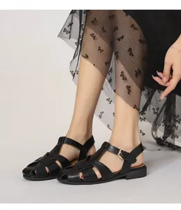 Details schwarzer geflochtener Römersandalen mit Goldschnalle an einem Model im Rock