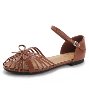 Brown flat sandals with woven hollow straps, bow accent, and buckle ankle closure