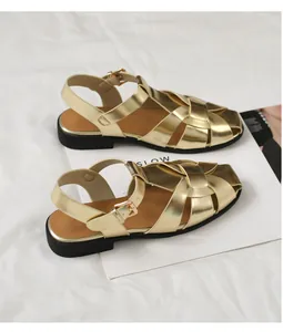 Makro-Detail goldener geflochtener Sandalen mit Metallschnalle und weicher brauner Sohle