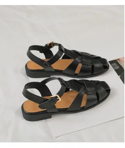 Detailansicht schwarzer geflochtener Römersandalen mit goldener Schnalle auf Stoff
