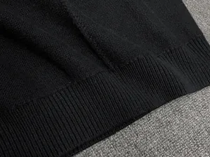 Detailed close-up showing the fine knit texture and ribbed hem of the black wool vest