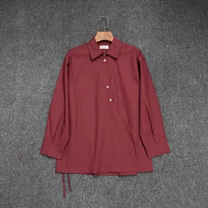 Detail of dark red cotton wrap shirt featuring asymmetrical lapels and white buttons