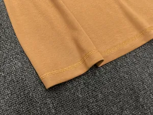 Detailed macro view of the double-stitched hem on a mustard yellow ribbed cotton vest
