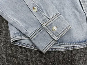 Detail view of light blue denim shirt cuff with white buttons and double stitching