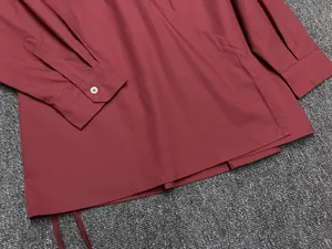 Detailed close-up of dark red cotton shirt showing white button and refined stitching