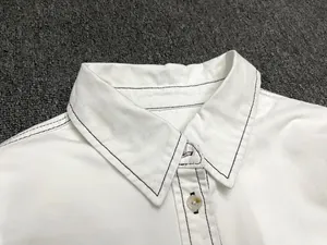 Detail of white cotton shirt collar with black contrast stitching and yellow buttons