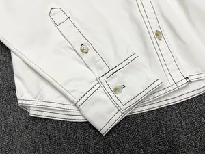 Close-up of white cotton shirt cuff with dark contrast stitching and amber buttons