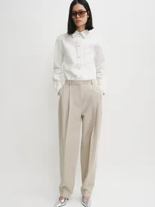 Minimalist white long sleeve shirt with contrast stitching and beige wide leg trousers