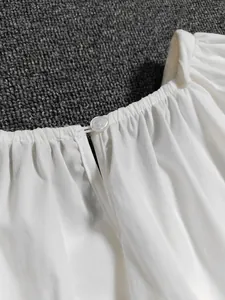 Détail de l'encolure d'un chemisier blanc avec des plis et un petit bouton élégant