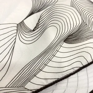 Detailed macro view of white silk scarf with black geometric wave pattern and hemmed edge