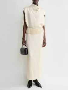 Detail of elegant cream sleeveless satin top with draped neckline and fringe waist tassels