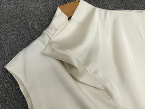 Detail of cream satin sleeveless top showing the high neck collar and silky texture